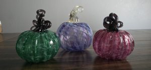3 blown glass pumpkins (green, purple, and pink) sitting on a table. 