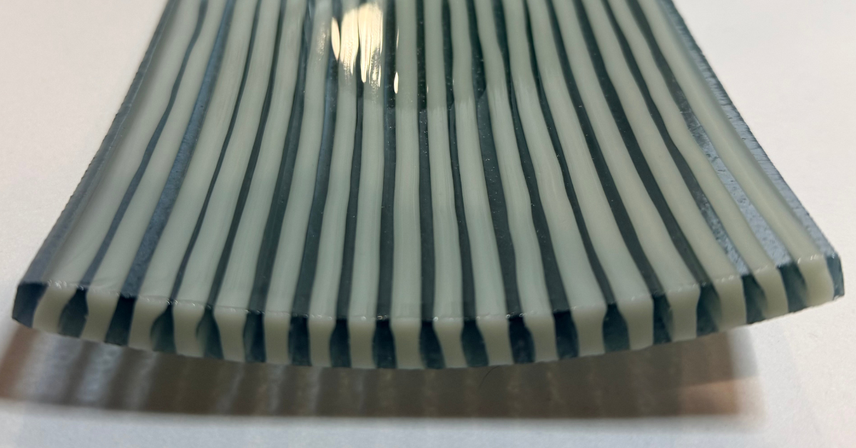 Close-up of a handmade fused glass artwork with alternating teal blue and white stripes, showing kiln-formed glass texture and curved design.